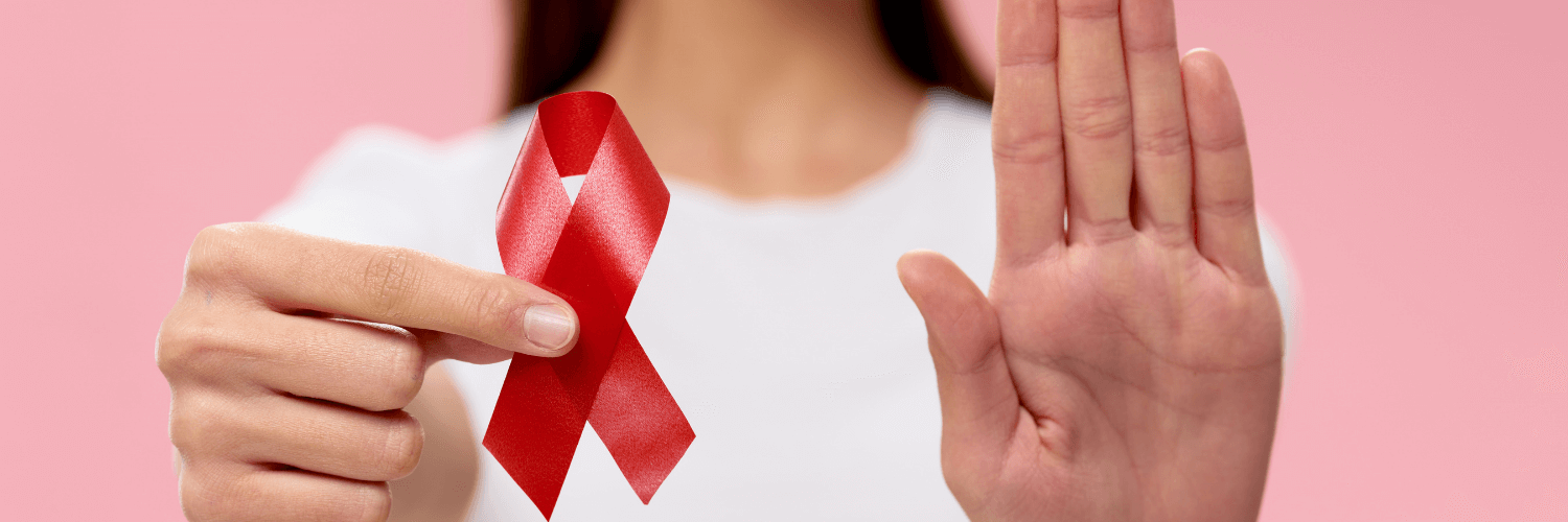 A woman holding her right hand up and her left hand is holding a pink breast cancer awareness ribbon